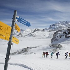 Gruppe von Schneeschuhläufer kämpft sich durch den Schnee, im Vordergrund steht ein Wegweiser | © Michi_Portmann